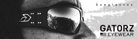 Close-up of a person wearing Gatorz sunglasses, reflecting a mountain landscape, with "Sunglasses" and "Gatorz Eyewear" text.